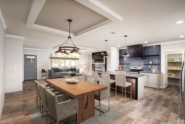 dining area with crown molding, a raised ceiling, a notable chandelier, and wood-type flooring