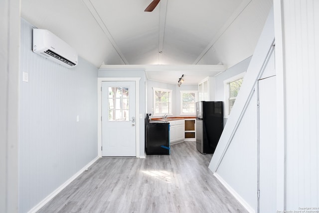 interior space with light hardwood / wood-style floors, lofted ceiling, stainless steel fridge, ceiling fan, and an AC wall unit