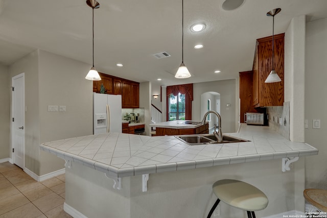 kitchen with kitchen peninsula, sink, decorative light fixtures, and white fridge with ice dispenser