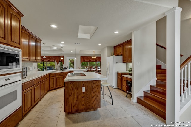 kitchen featuring a kitchen island, decorative light fixtures, white appliances, light tile patterned floors, and sink