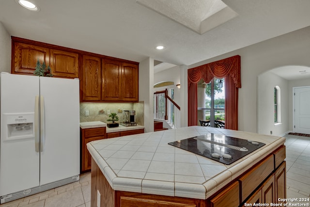 kitchen featuring a center island, tile countertops, white refrigerator with ice dispenser, black electric stovetop, and tasteful backsplash