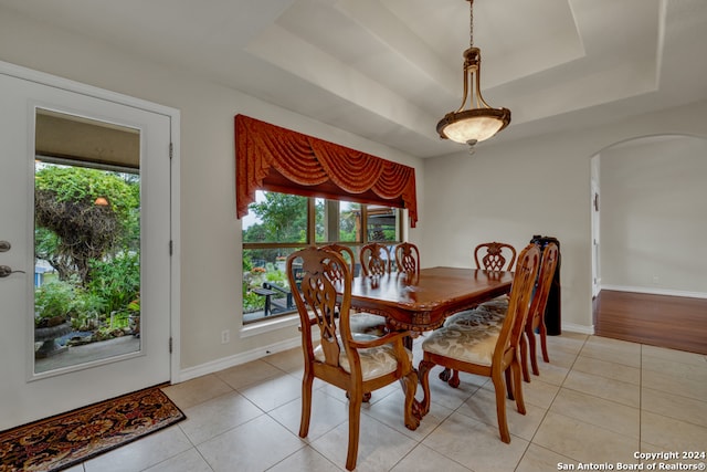 dining space with a tray ceiling and light tile patterned flooring