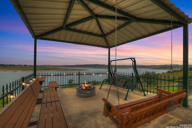 deck at dusk featuring an outdoor fire pit, a water view, and a gazebo