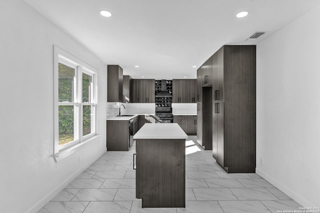 kitchen with dark brown cabinetry, sink, wall chimney range hood, black gas range, and a kitchen island