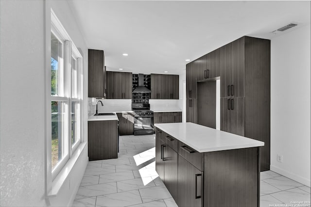 kitchen featuring gas stove, sink, wall chimney range hood, decorative backsplash, and a kitchen island