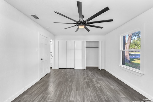 unfurnished bedroom featuring ceiling fan, dark wood-type flooring, and multiple closets