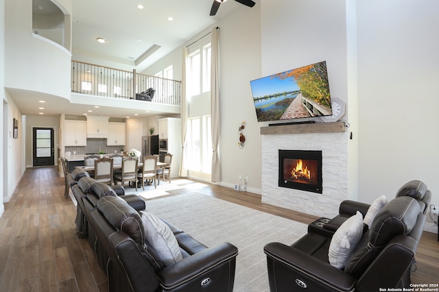 living room with a towering ceiling, ceiling fan, hardwood / wood-style flooring, and a stone fireplace