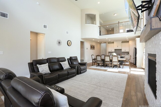 living room with light wood-type flooring, a fireplace, and a high ceiling