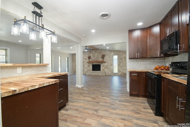 kitchen with pendant lighting, light hardwood / wood-style flooring, butcher block countertops, black appliances, and a stone fireplace