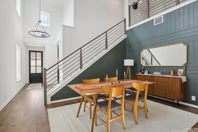 dining space featuring a high ceiling, wood walls, wood-type flooring, and a chandelier