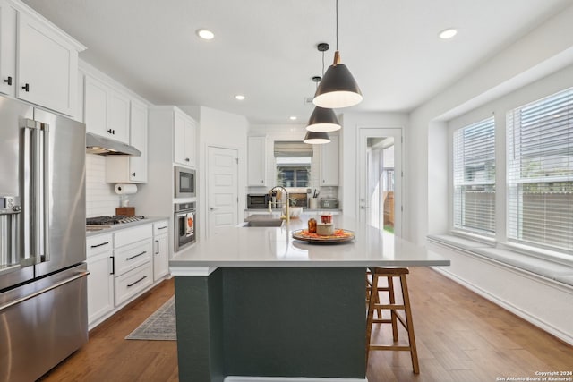 kitchen with appliances with stainless steel finishes, hanging light fixtures, a kitchen island with sink, and wood-type flooring