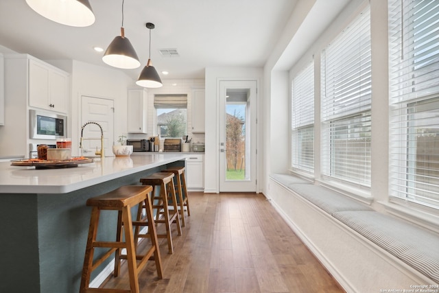 kitchen featuring decorative light fixtures, built in microwave, wood-type flooring, a large island with sink, and white cabinets