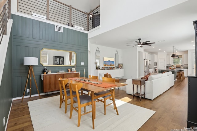 dining space featuring a towering ceiling, hardwood / wood-style flooring, ceiling fan, and wooden walls