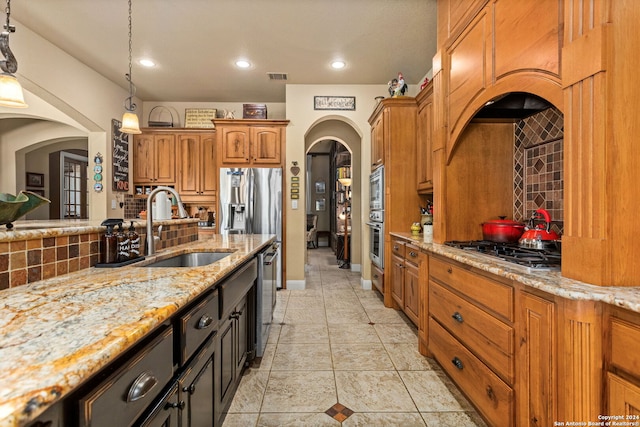 kitchen featuring decorative backsplash, stainless steel appliances, sink, light stone countertops, and decorative light fixtures