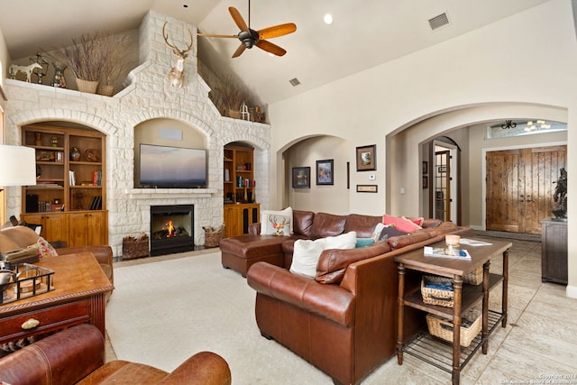 living room with built in features, a stone fireplace, high vaulted ceiling, and ceiling fan