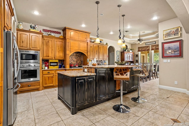 kitchen featuring ceiling fan, stainless steel appliances, pendant lighting, a breakfast bar, and a center island with sink