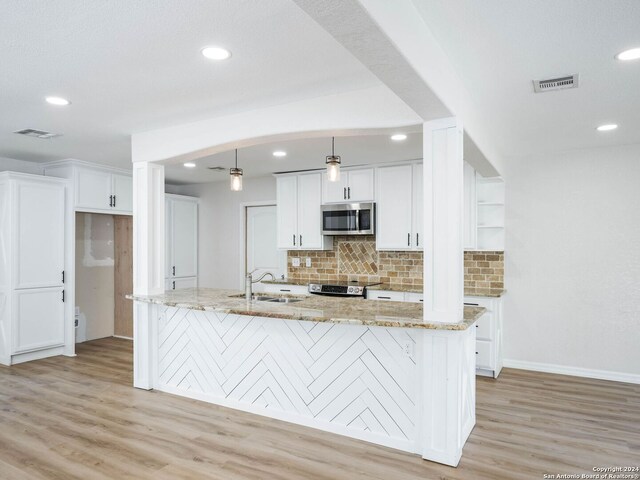 kitchen with stainless steel appliances, light stone counters, white cabinets, and light hardwood / wood-style floors