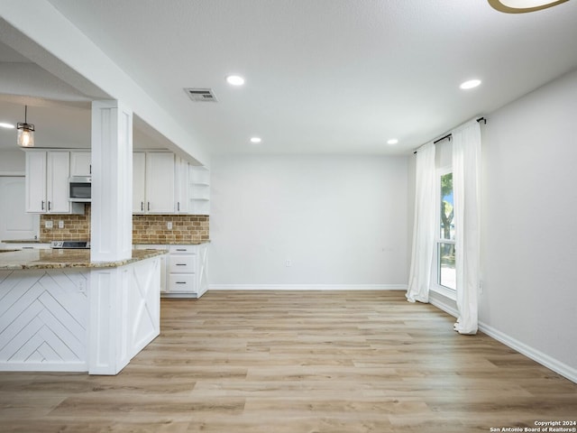 kitchen with white cabinets, hanging light fixtures, light wood-type flooring, light stone counters, and tasteful backsplash