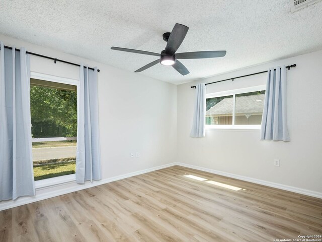 empty room featuring a healthy amount of sunlight, ceiling fan, and light hardwood / wood-style flooring