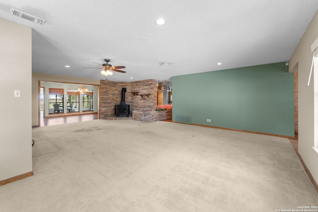 unfurnished living room featuring carpet flooring, ceiling fan with notable chandelier, a wood stove, and a textured ceiling