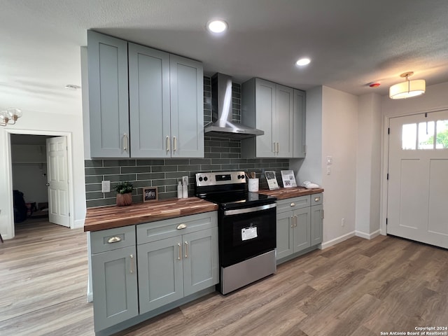 kitchen with gray cabinetry, butcher block countertops, wall chimney exhaust hood, stainless steel electric range oven, and light wood-type flooring