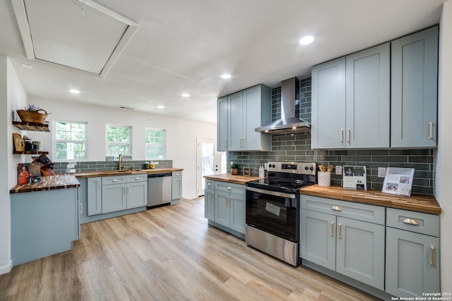 kitchen featuring light hardwood / wood-style flooring, wood counters, stainless steel appliances, sink, and wall chimney range hood