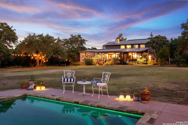 pool at dusk with a lawn and a patio area