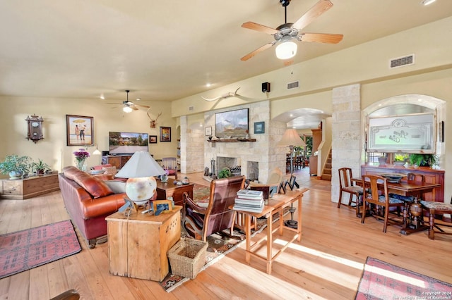 living room featuring light hardwood / wood-style flooring, ceiling fan, and a stone fireplace