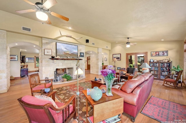 living room featuring light hardwood / wood-style flooring, ceiling fan, and a stone fireplace