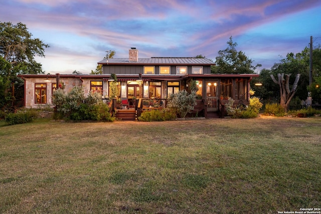 back house at dusk with a yard and a sunroom