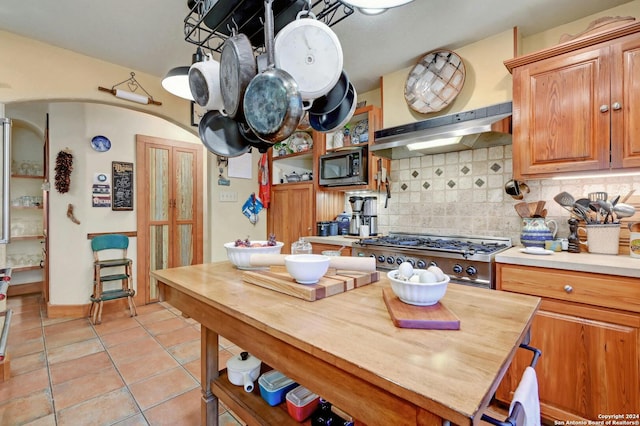 kitchen featuring butcher block countertops, stainless steel appliances, range hood, decorative backsplash, and light tile patterned flooring