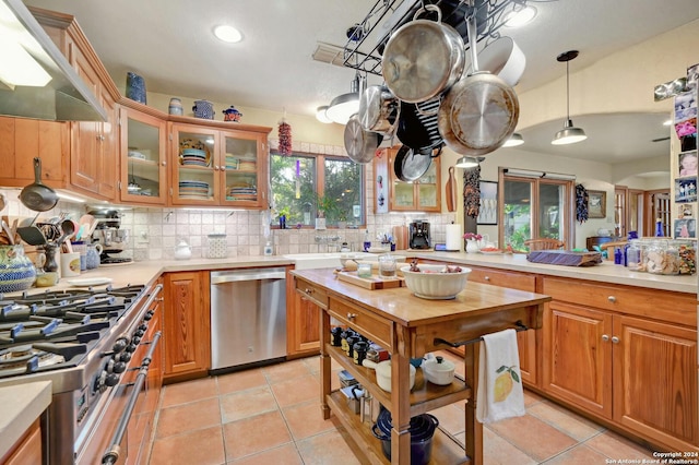 kitchen with decorative backsplash, stainless steel appliances, light tile patterned flooring, pendant lighting, and exhaust hood