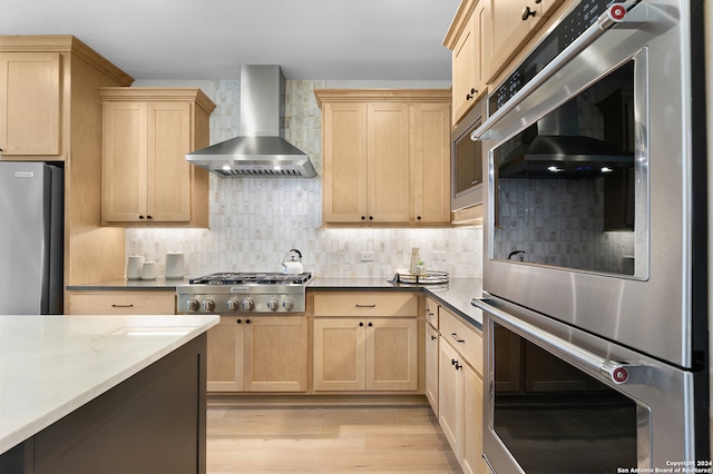 kitchen featuring light brown cabinetry, stainless steel appliances, decorative backsplash, wall chimney range hood, and light wood-type flooring