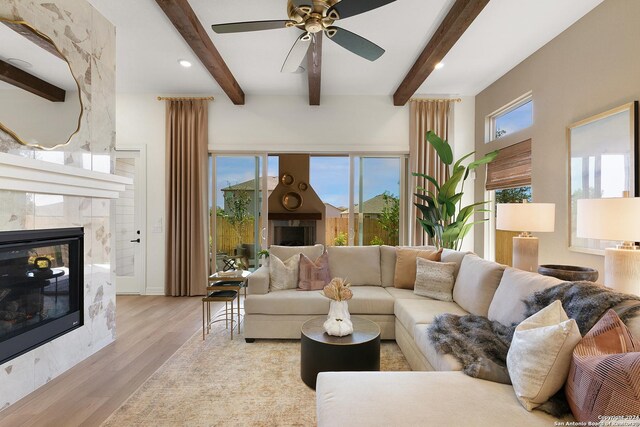 living room featuring ceiling fan, a fireplace, light hardwood / wood-style floors, and beamed ceiling