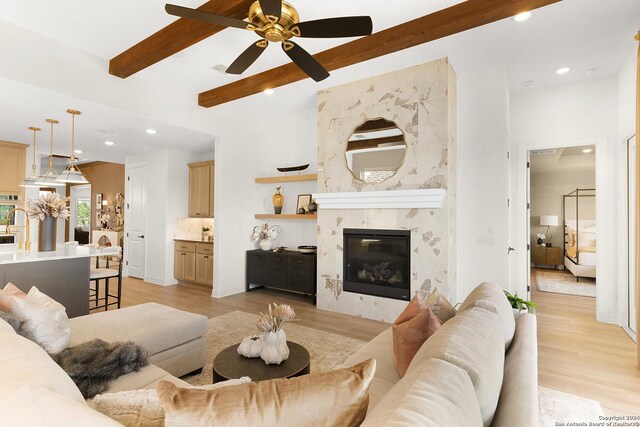 living room featuring light wood-type flooring, ceiling fan, beamed ceiling, and a premium fireplace