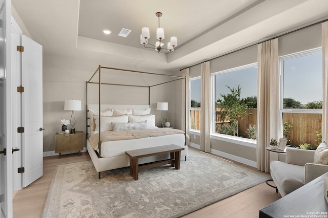 bedroom featuring a tray ceiling, a notable chandelier, and light hardwood / wood-style floors