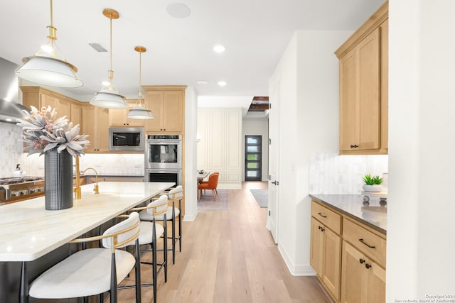 kitchen with light hardwood / wood-style flooring, pendant lighting, light brown cabinetry, appliances with stainless steel finishes, and decorative backsplash