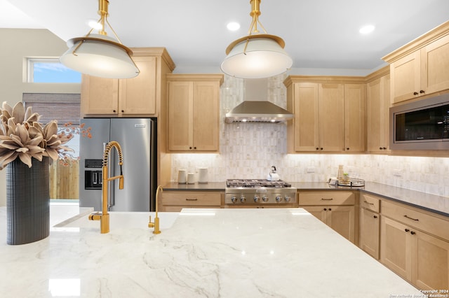 kitchen with pendant lighting, stainless steel appliances, wall chimney exhaust hood, and light brown cabinetry