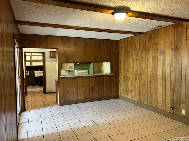 kitchen with kitchen peninsula, light tile patterned floors, a textured ceiling, beam ceiling, and wooden walls