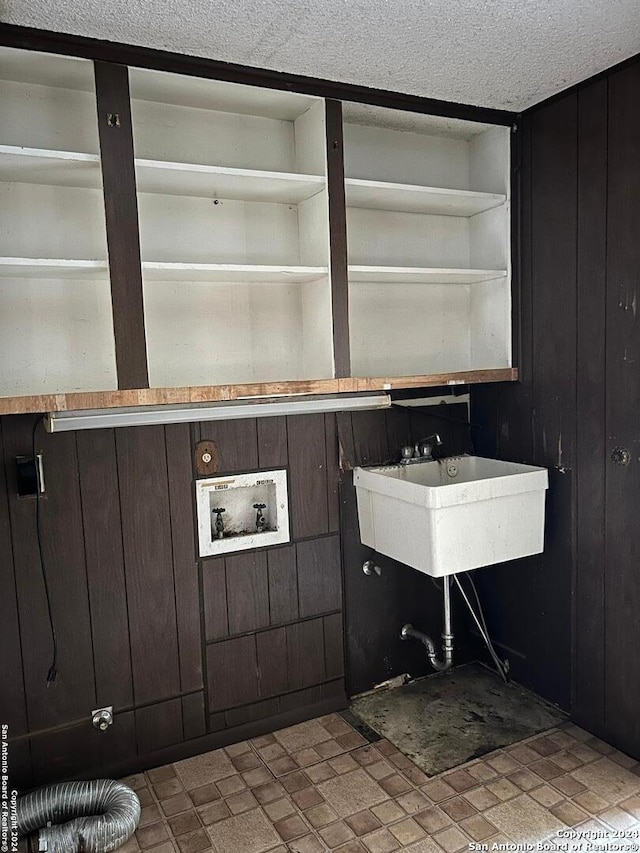 bathroom with a textured ceiling, wooden walls, and sink