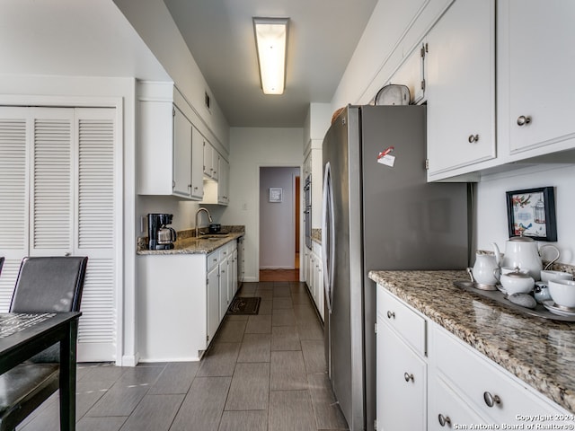 kitchen with stainless steel fridge, white cabinetry, sink, and light stone countertops