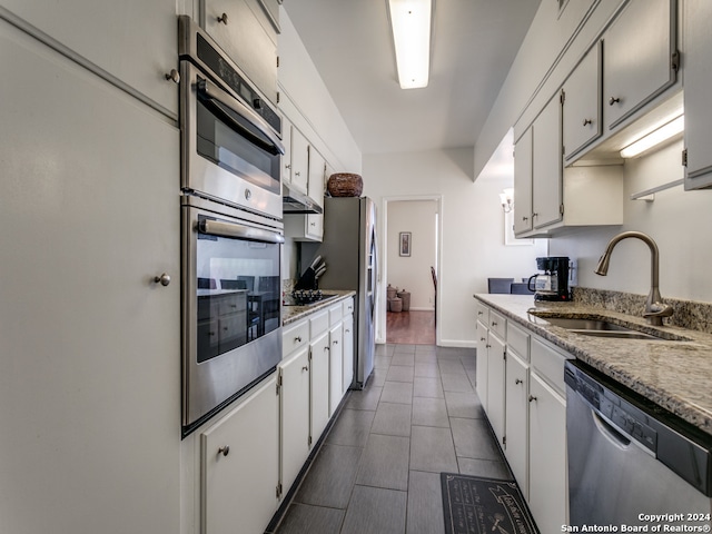 kitchen with light stone countertops, stainless steel appliances, white cabinetry, sink, and dark hardwood / wood-style floors