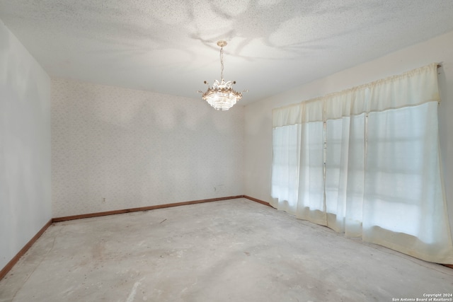 unfurnished room featuring concrete floors, a notable chandelier, and a textured ceiling