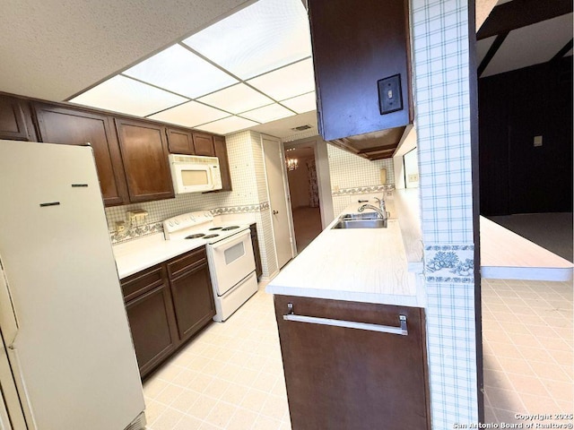 kitchen with dark brown cabinetry, sink, backsplash, and white appliances