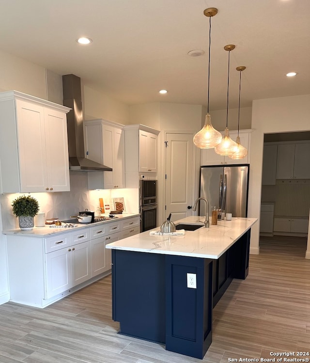 kitchen with an island with sink, stainless steel appliances, wall chimney range hood, and white cabinets