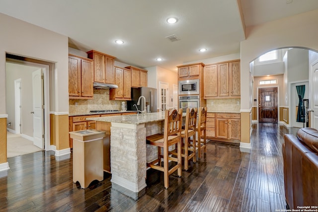 kitchen featuring a breakfast bar area, dark hardwood / wood-style floors, backsplash, an island with sink, and stainless steel appliances