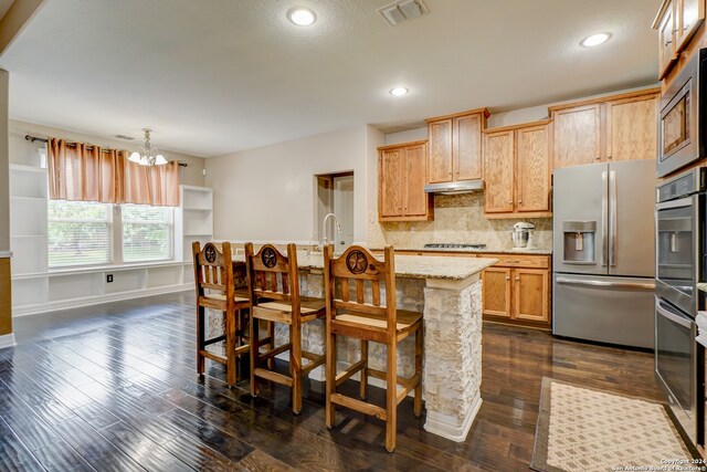 kitchen with decorative light fixtures, a notable chandelier, appliances with stainless steel finishes, dark wood-type flooring, and a breakfast bar