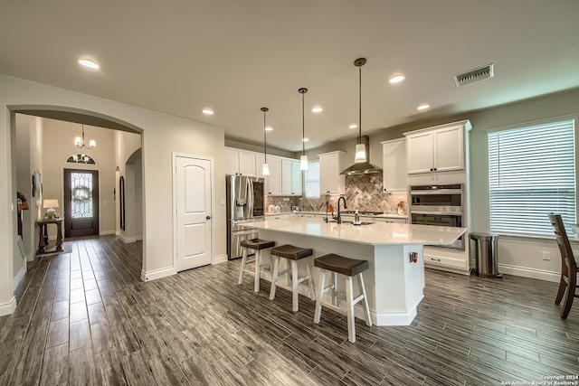 kitchen with a center island with sink, appliances with stainless steel finishes, white cabinets, and wall chimney exhaust hood