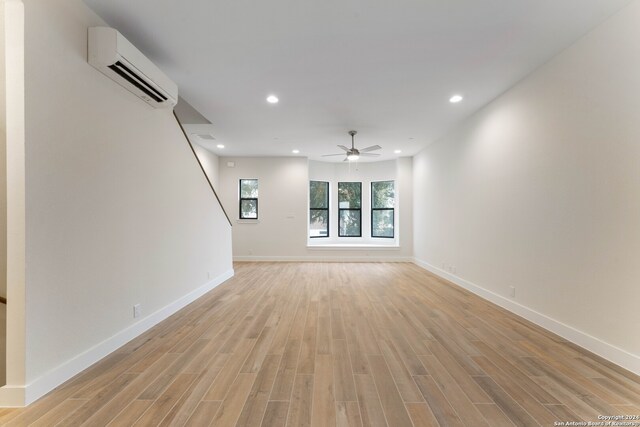 unfurnished living room with ceiling fan, recessed lighting, baseboards, a wall mounted AC, and light wood-type flooring