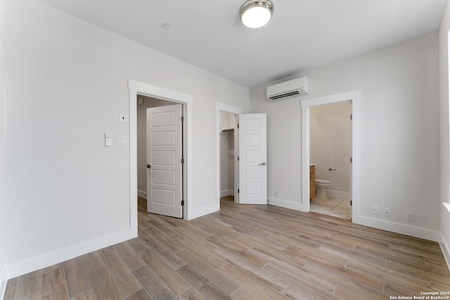 unfurnished bedroom with a spacious closet, light wood-style flooring, a wall mounted AC, connected bathroom, and baseboards